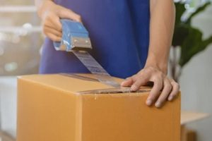 focus hand of asian woman, female holding packing, unpacking box by tape machine